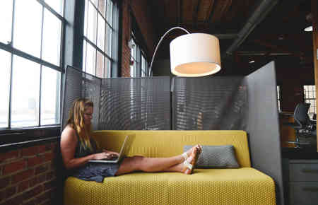 Junge Frau arbeitet flexibel auf einem Sofa mit Laptop in einem modernen Büro